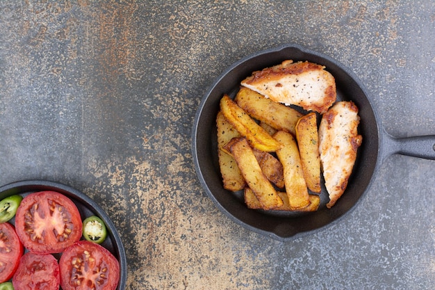 Pollo asado y patatas en sartén con plato de verduras. Foto de alta calidad