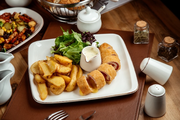 Pollo cordon bleu con papas en ensalada rural y salsa en un plato