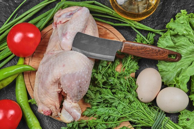 Pollo crudo en placa de madera con un montón de verduras frescas.