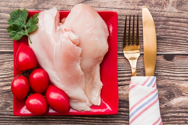 Pollo crudo y tomates en plato con tenedor y cuchillo