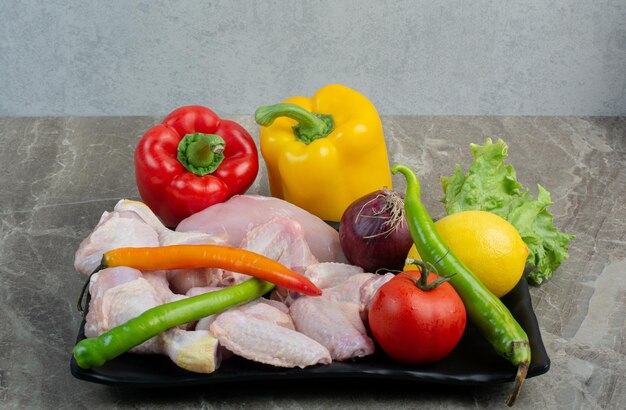 Pollo crudo con verduras en un plato oscuro. Foto de alta calidad