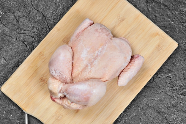 Foto gratuita pollo entero crudo sobre una tabla de cortar de madera