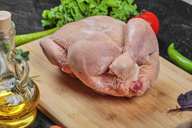 Pollo entero crudo sobre tabla de madera con aceite y tomates