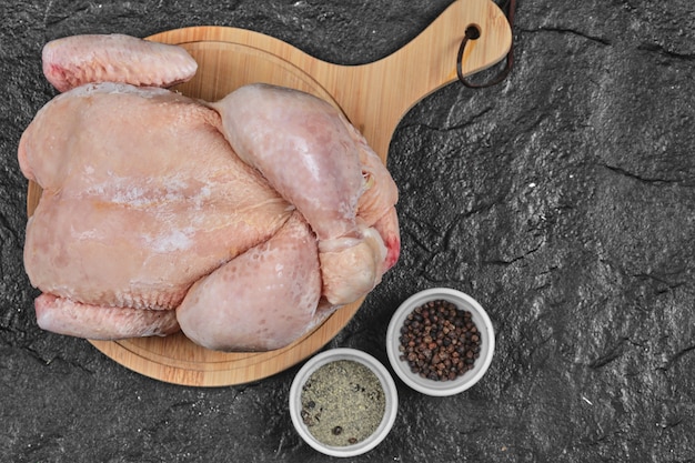 Foto gratuita pollo entero crudo sobre tabla de madera con especias