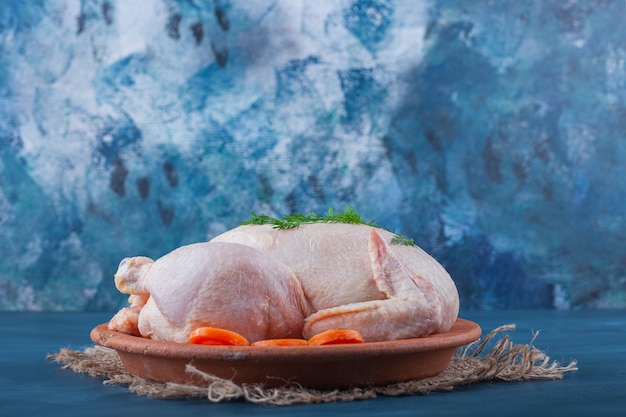 Foto gratuita pollo entero y zanahorias en rodajas en un plato sobre una servilleta de arpillera sobre la superficie azul