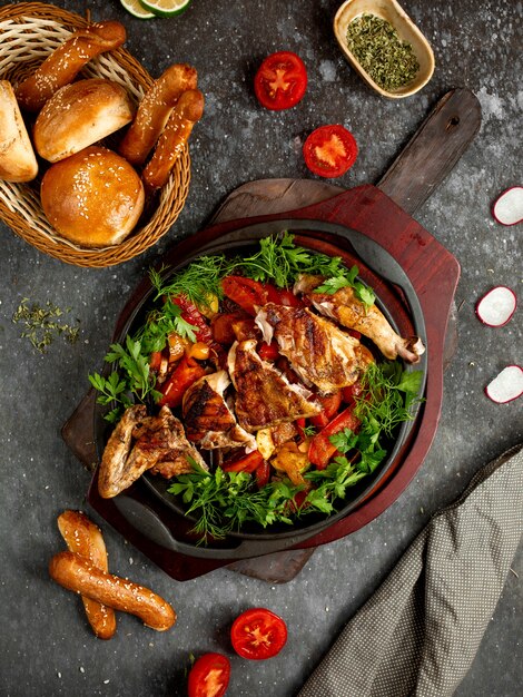 Pollo frito con verduras y hierbas en una sartén de aluminio.