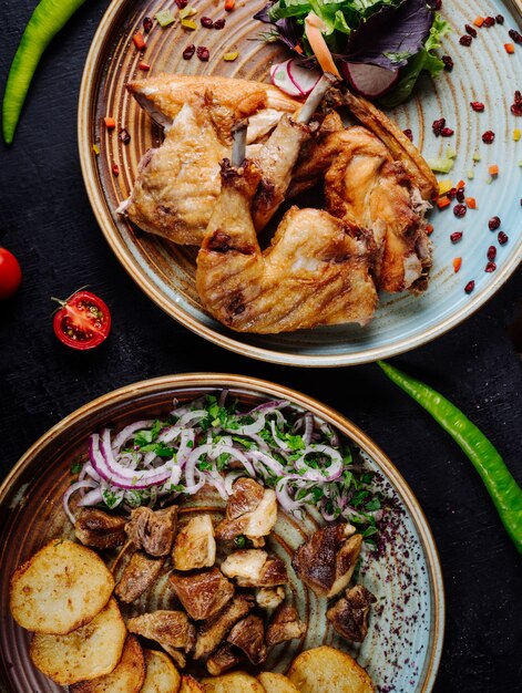 Pollo a la parrilla, estofado de ternera y papas fritas con cebolla y ensalada verde en platos.