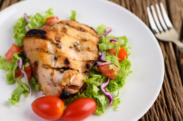 Pollo a la parrilla en un plato blanco con una ensalada de tomates, zanahorias y chiles cortados en trozos.