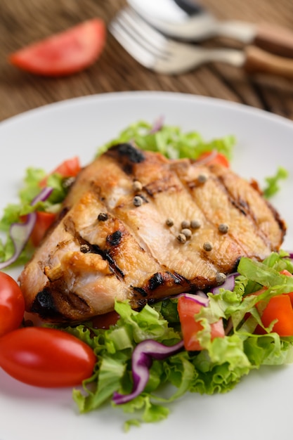 Foto gratuita pollo a la parrilla en un plato blanco con una ensalada de tomates, zanahorias y chiles cortados en trozos.