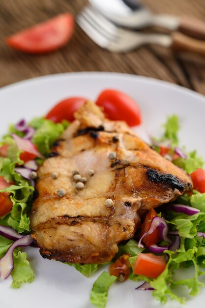 Pollo a la parrilla en un plato blanco con una ensalada de tomates, zanahorias y chiles cortados en trozos.