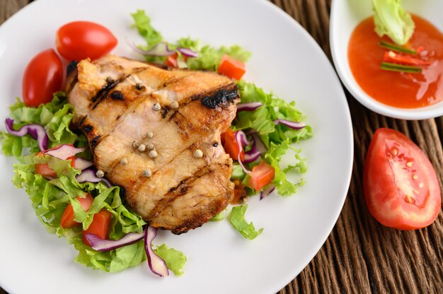 Pollo a la parrilla en un plato blanco con una ensalada de tomates, zanahorias y chiles cortados en trozos.