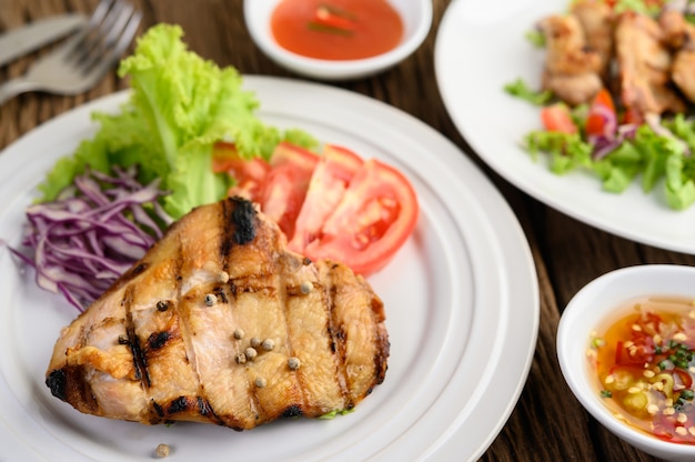 Pollo a la parrilla en un plato blanco con una ensalada de tomates, zanahorias y chiles cortados en trozos.