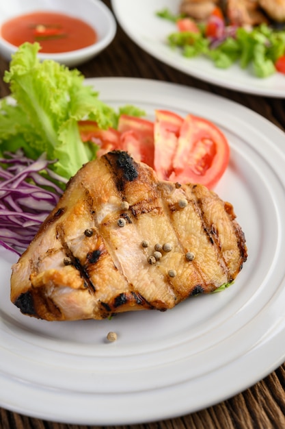 Pollo a la parrilla en un plato blanco con una ensalada de tomates, zanahorias y chiles cortados en trozos.