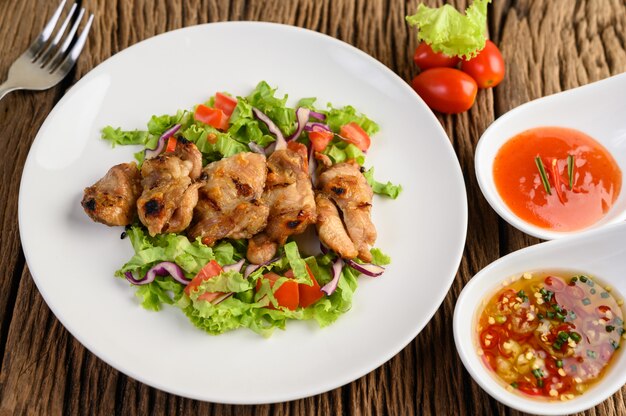 Pollo a la parrilla en un plato blanco con una ensalada de tomates, zanahorias y chiles cortados en trozos.