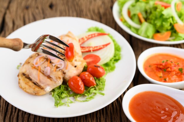 Pollo a la parrilla en un plato blanco con tomate, ensalada, cebolla, chile y salsa. Seleccione tomate en tenedor de brocheta.