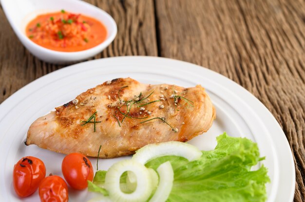 Pollo a la parrilla en un plato blanco con tomate, ensalada, cebolla, chile y salsa.