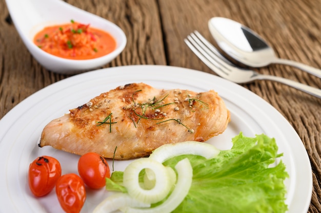 Pollo a la parrilla en un plato blanco con tomate, ensalada, cebolla, chile y salsa.