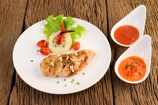 Pollo a la parrilla en un plato blanco con tomate, ensalada, cebolla, chile y salsa.