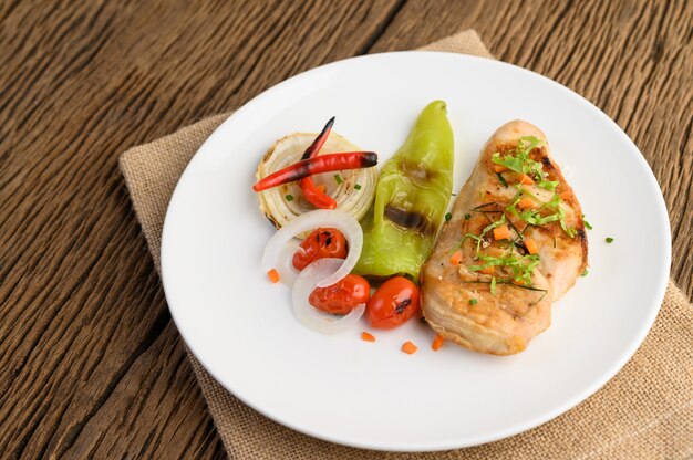 Pollo a la parrilla en un plato blanco con tomate, ensalada, cebolla, chile y salsa.