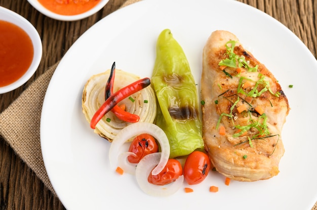 Pollo a la parrilla en un plato blanco con tomate, ensalada, cebolla, chile y salsa.