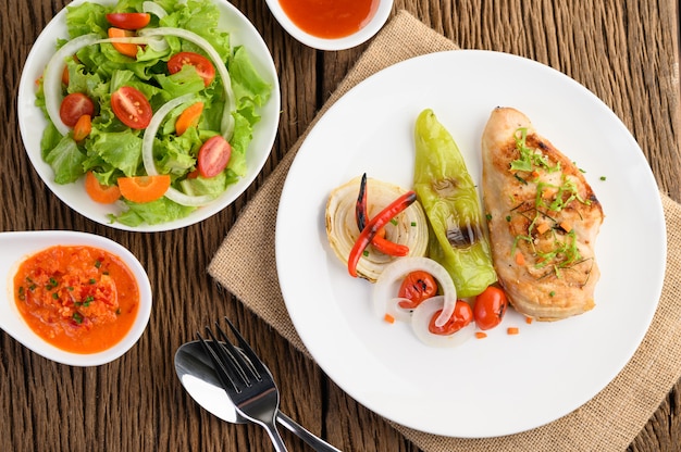 Pollo a la parrilla en un plato blanco con tomate, ensalada, cebolla, chile y salsa.