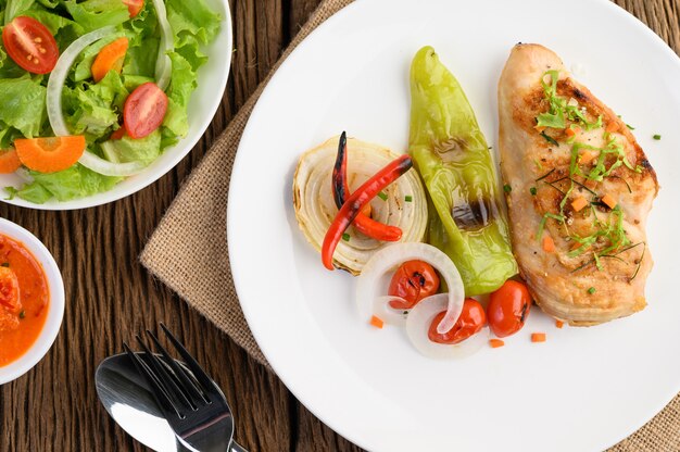 Pollo a la parrilla en un plato blanco con tomate, ensalada, cebolla, chile y salsa.