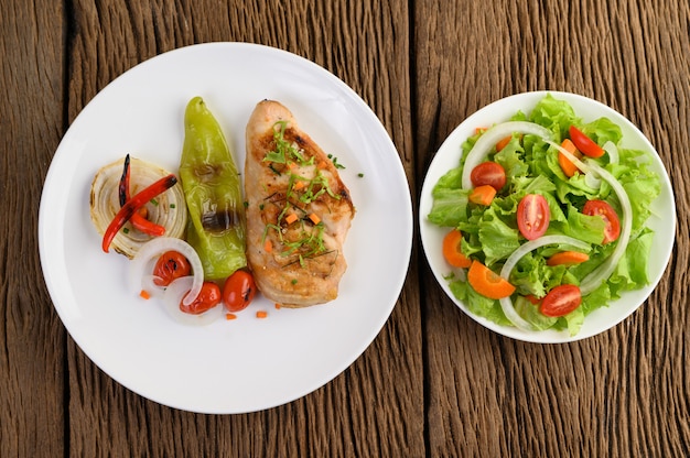 Pollo a la parrilla en un plato blanco con tomate, ensalada, cebolla, chile y salsa.