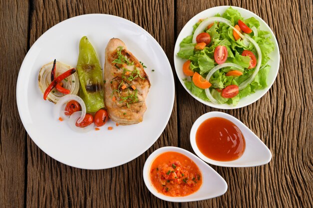 Pollo a la parrilla en un plato blanco con tomate, ensalada, cebolla, chile y salsa.