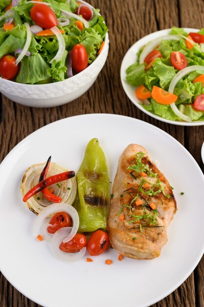 Pollo a la parrilla en un plato blanco con tomate, ensalada, cebolla, chile y salsa.