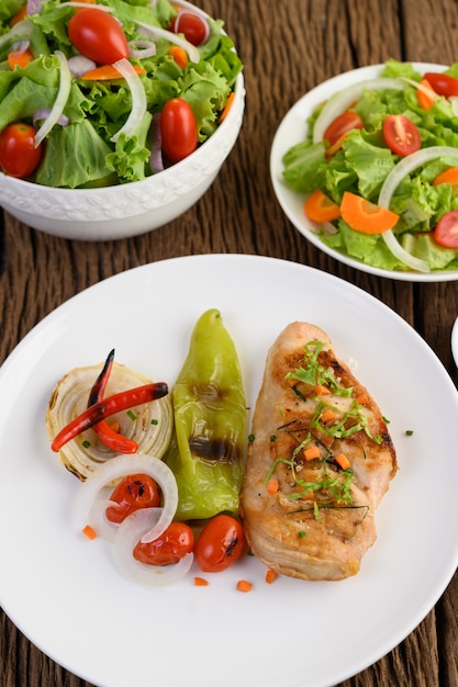 Pollo a la parrilla en un plato blanco con tomate, ensalada, cebolla, chile y salsa.