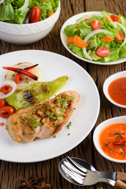 Pollo a la parrilla en un plato blanco con tomate, ensalada, cebolla, chile y salsa.