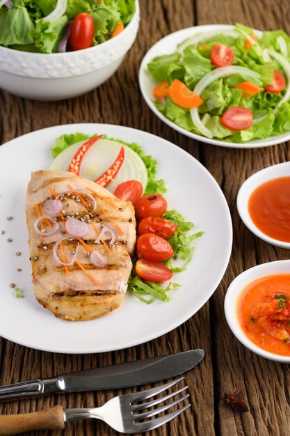 Pollo a la parrilla en un plato blanco con tomate, ensalada, cebolla, chile y salsa.