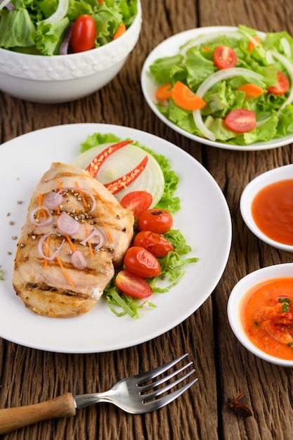 Pollo a la parrilla en un plato blanco con tomate, ensalada, cebolla, chile y salsa.