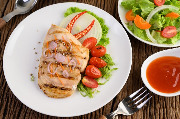 Pollo a la parrilla en un plato blanco con tomate, ensalada, cebolla, chile y salsa.