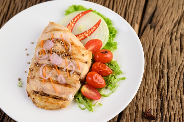 Pollo a la parrilla en un plato blanco con tomate, ensalada, cebolla, chile y salsa.