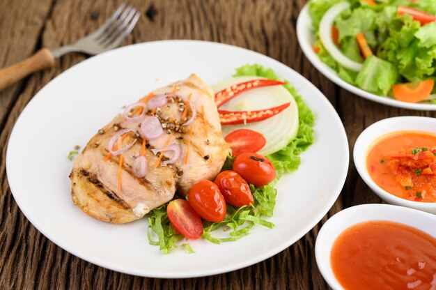 Pollo a la parrilla en un plato blanco con tomate, ensalada, cebolla, chile y salsa.