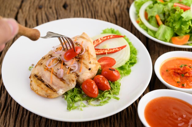 Pollo a la parrilla en un plato blanco con tomate, ensalada, cebolla, chile y salsa.