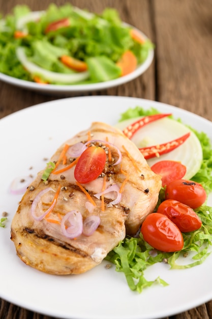 Pollo a la parrilla en un plato blanco con tomate, ensalada, cebolla, chile y salsa.