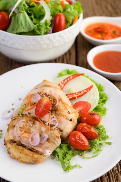 Pollo a la parrilla en un plato blanco con tomate, ensalada, cebolla, chile y salsa.