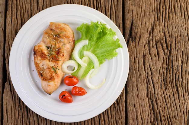 Pollo a la parrilla en un plato blanco con tomate, ensalada y cebolla.