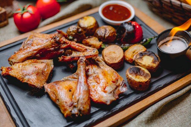 Pollo a la parrilla sobre tabla de madera papa tomate pimiento salsa de chile vista lateral