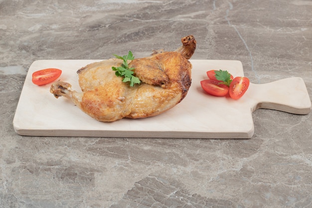 Pollo a la plancha sobre tabla de madera con rodajas de tomate.