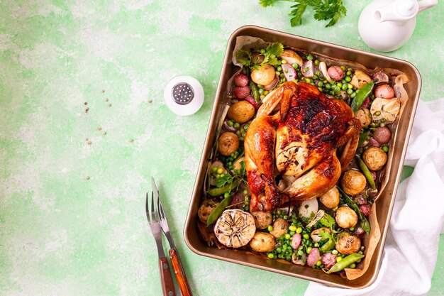 Pollo de primavera horneado con rábanos y guisantes verdes en una olla sobre un fondo verde