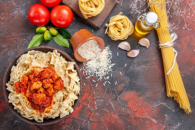 Pollo de vista superior con plato de pasta de masa con tomates en harina de pasta de masa de superficie oscura