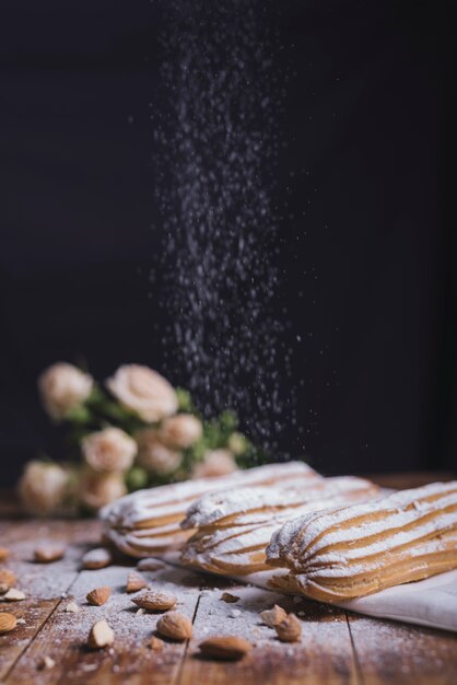 Polvo de azúcar en polvo en el eclair horneado con almendras sobre fondo negro