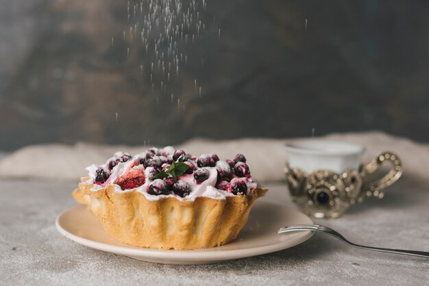 Polvo de azúcar en tarta de frutas con bayas en un plato de cerámica