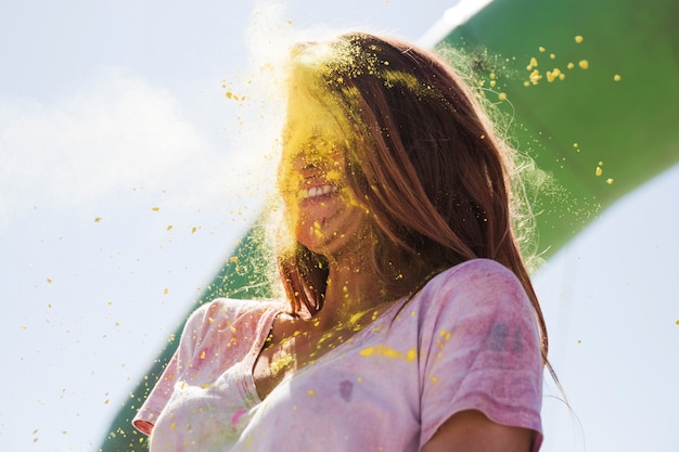 Foto gratuita polvo de color holi amarillo explota en la cara de la mujer.