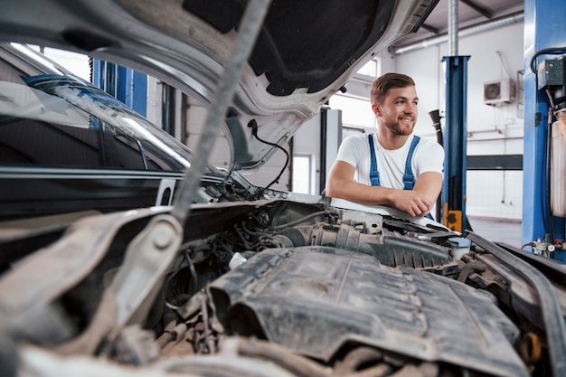 Polvo en el motor. Empleado en el uniforme de color azul trabaja en el salón del automóvil