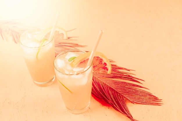 Pomelo frío y cóctel de naranja en dos vasos con cubitos de hielo sobre fondo de color