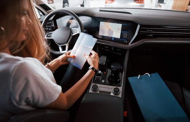 Pon tu texto aquí. Chica en coche moderno en el salón. Durante el día en interiores. Comprar vehículo nuevo